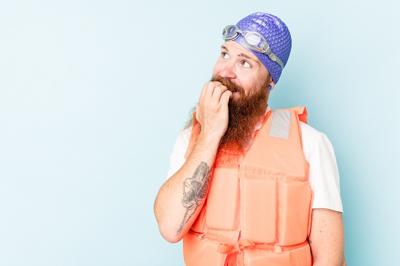Young caucasian man wearing life jacket isolated on blue background relaxed thinking about something looking at a copy space.